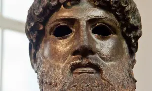 Tête en bronze de Zeus, dieu de la foudre, avec une barbe et des cheveux bouclés. Son regard est intense, prêt à lancer ses éclairs.