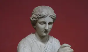 Buste en marbre d'une femme, peut-être Calliope, muse de la mythologie grecque, sur fond rouge.