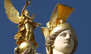 Statue dorée d'une déesse de la guerre ailée, tenant une couronne et une lance, perchée sur une sphère. Une autre tête de déesse ornée d'un casque doré est visible.