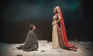 Sur scène, une femme agenouillée, drapée de noir, implore une figure royale vêtue d'or et de rouge. Une scène du mythe d'Électre.