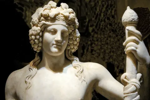 Sculpture de marbre d'une déesse du vin, couronnée de grappes de raisin, tenant un bâton orné.
