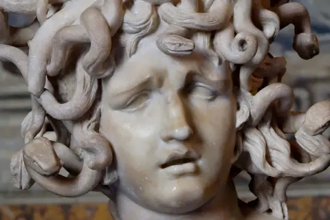 Sculpture de la gorgone mythologie, son visage figé dans une expression de douleur, ses cheveux remplacés par des serpents enroulés.