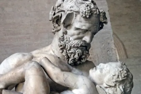 Sculpture d'un homme barbu portant un enfant, évoquant la **mythologie** de **Zagreus**. L'homme, couronné de pampres, serre tendrement le petit corps.