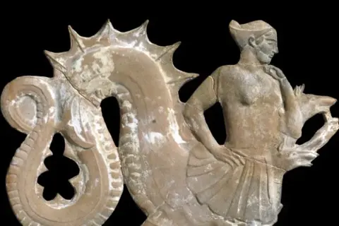 Figurine en terre cuite représentant un homme aux côtés d'une créature marine, évoquant la **charybde mythologie**.