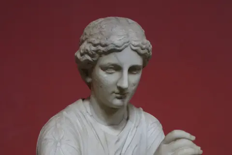 Buste en marbre d'une femme, peut-être Calliope, muse de la mythologie grecque, sur fond rouge.