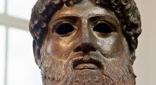 Tête en bronze de Zeus, dieu de la foudre, avec une barbe et des cheveux bouclés. Son regard est intense, prêt à lancer ses éclairs.