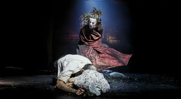 Sur scène, une figure tourmentée, peut-être Clytemnestre, domine deux hommes à terre. La tragédie des Atrides se joue dans l'ombre.