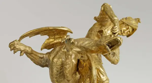 Statue dorée d'un guerrier combattant un dragon, évoquant le roi mythique d'Iolcos. Le guerrier, casqué, saisit la gueule ouverte de la créature ailée.