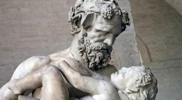 Sculpture d'un homme barbu portant un enfant, évoquant la **mythologie** de **Zagreus**. L'homme, couronné de pampres, serre tendrement le petit corps.