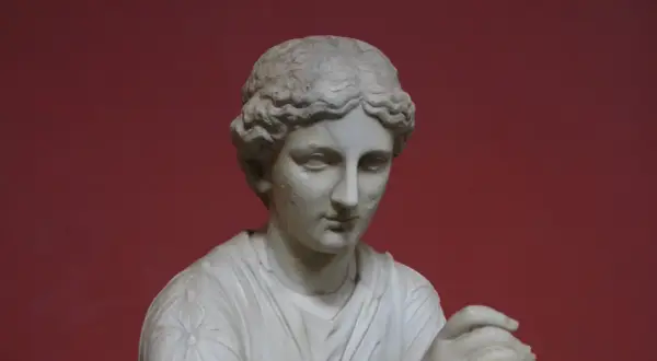 Buste en marbre d'une femme, peut-être Calliope, muse de la mythologie grecque, sur fond rouge.