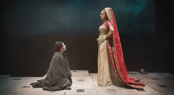 Sur scène, une femme agenouillée, drapée de noir, implore une figure royale vêtue d'or et de rouge. Une scène du mythe d'Électre.