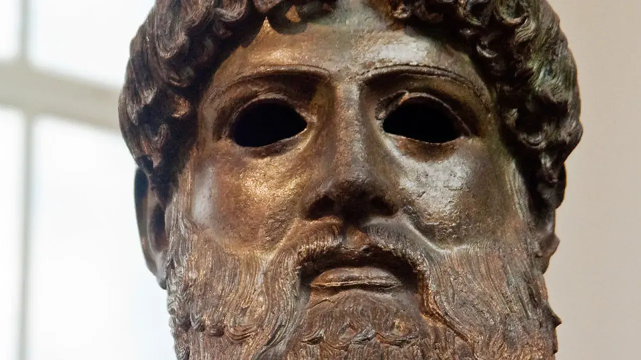 Tête en bronze de Zeus, dieu de la foudre, avec une barbe et des cheveux bouclés. Son regard est intense, prêt à lancer ses éclairs.