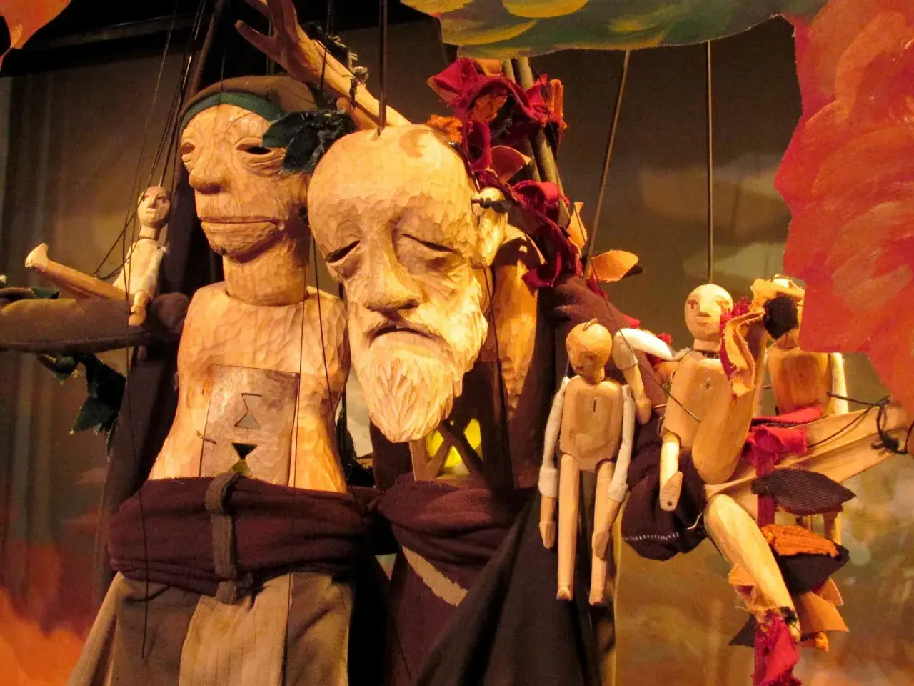 Marionnettes en bois sculpté, évoquant Philémon et Baucis, avec des visages expressifs et des corps articulés, suspendues par des fils.