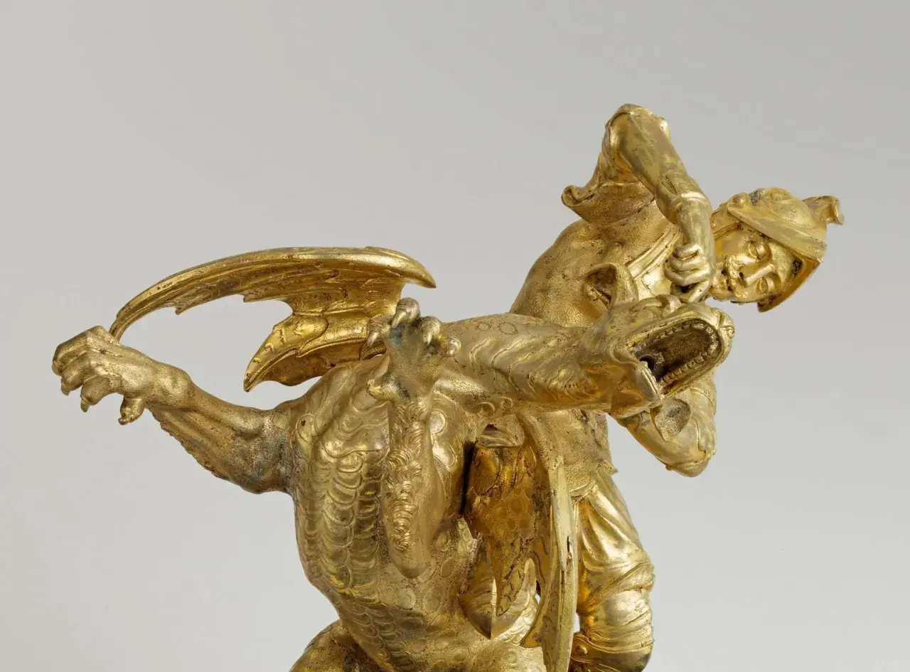 Statue dorée d'un guerrier combattant un dragon, évoquant le roi mythique d'Iolcos. Le guerrier, casqué, saisit la gueule ouverte de la créature ailée.