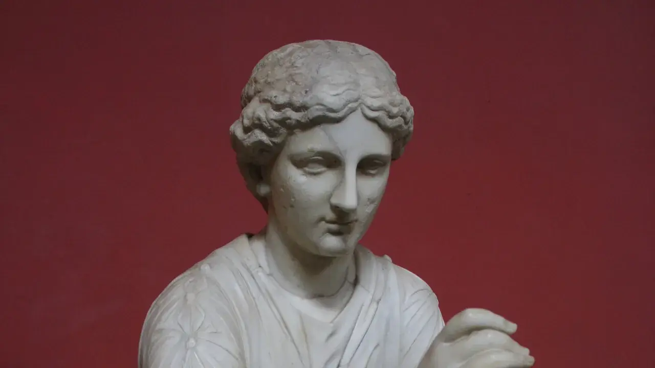 Buste en marbre d'une femme, peut-être Calliope, muse de la mythologie grecque, sur fond rouge.