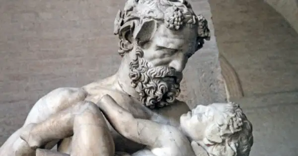 Sculpture d'un homme barbu portant un enfant, évoquant la **mythologie** de **Zagreus**. L'homme, couronné de pampres, serre tendrement le petit corps.
