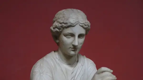 Buste en marbre d'une femme, peut-être Calliope, muse de la mythologie grecque, sur fond rouge.